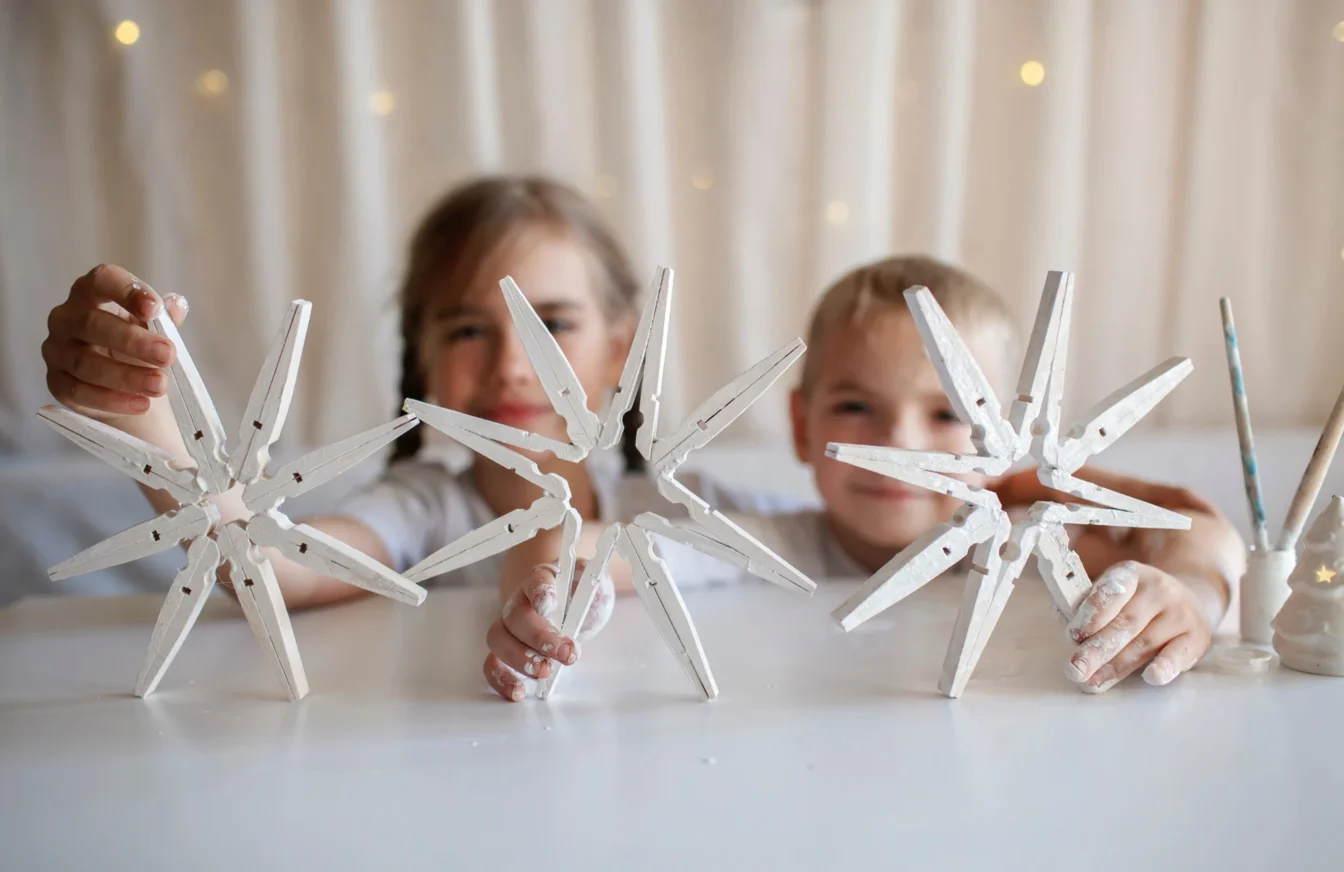 Imagen de un niño y una niña jugando mientras muestran unas estrellas navideñas realizadas con pinzas de madera para tender la ropa pintadas de blanco