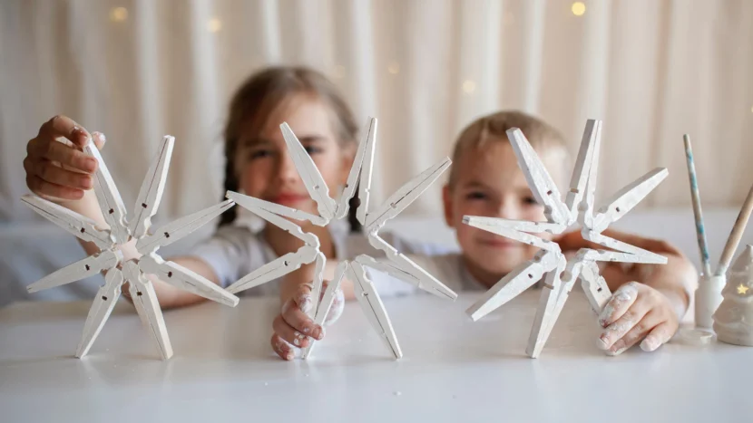 Imagen de un niño y una niña jugando mientras muestran unas estrellas navideñas realizadas con pinzas de madera para tender la ropa pintadas de blanco